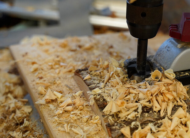 Löcher werden mit einem Standbohrer in ein Holzbrett gebohrt.