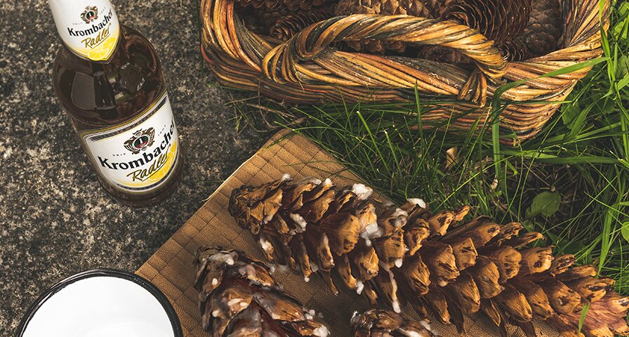 Ein Krombacher Radler und zwei Tannenzapfen und eine Korb ist zu sehen.