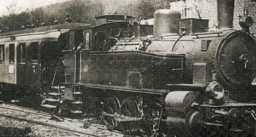  Historische Aufnahme einer Dampflok mit Waggon auf Gleisen.