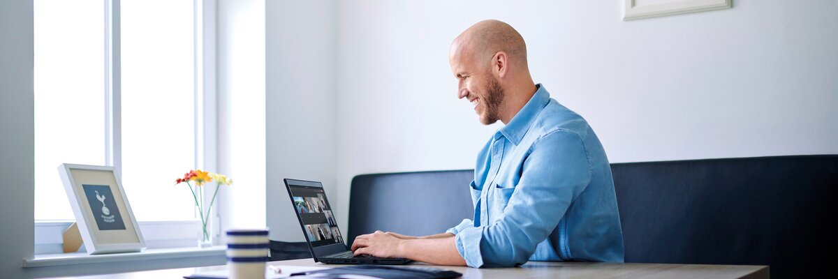 Ein Mann mit Glatze sitzt an einem Tisch und arbeitet an einem Laptop. Er trägt ein hellblaues Hemd. 