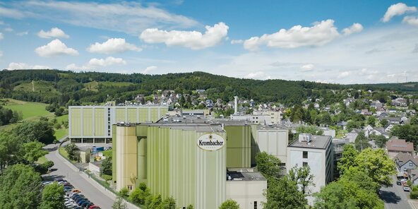 Luftaufnahme der Krombacher Brauerei mit grüner und gelber Fassadenfarbe, umgeben von Bäumen und Wohngebieten.