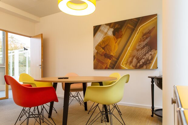 Ein Konferenzraum mit einem runden Tisch, umgeben von vier Stühlen in Rot, Gelb und Beige. 