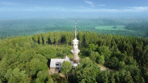 Luftaufnahme des Kindelsturms im Waldgebiet. Der Turm ist hoch und hat eine Antenne oben. 