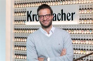 Mann mit dunkelbraunen Haaren trägt eine Brille und einen grauen Pullover. Er lächelt in die Kamera.