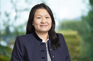 Frau mit schwarzen, langen Haaren, trägt eine schwarze Jacke und lächelt in die Kamera.