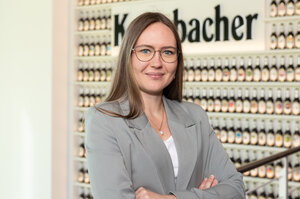 Frau mit langen, glatten braunen Haaren trägt eine Brille und einen hellgrauen Blazer.