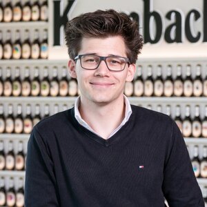 Mann mit kurzen braunen Haaren, trägt eine Brille und einen schwarzen Pullover. Er lächelt in die Kamera.