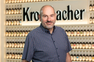 Mann mit kurzen grauen Haaren trägt ein blau kariertes Hemd und lächelt in die Kamera.