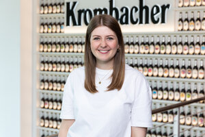 Frau mit langen, dunkelblonden Haaren trägt ein weißes T-Shirt. Sie lächelt in die Kamera.