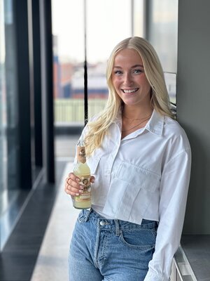 Junge Frau mit langen blonden Haaren trägt ein weißes Hemd und lächelt in die Kamera.