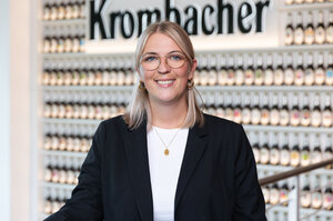 Frau mit langen, blonden Haaren trägt eine schwarzen Blazer und eine Brille. Sie lächelt in die Kamera.