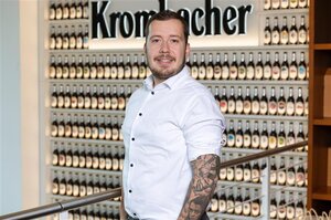 Mann mit tätowiertem Arm in weißem Hemd, lächelt in die Kamera.