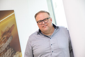 Ein Mann mit blond-grauen Haaren, trägt ein graues Hemd und lächelt in die Kamera.