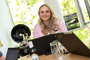 Frau mit blonden, leicht gelockten Haaren trägt eine rosa-weiß gestreifte Bluse und lächelt in die Kamera.