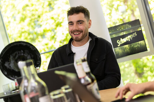 Mann mit schwarzem Hemd sitzt an einem Tisch und lächelt.
