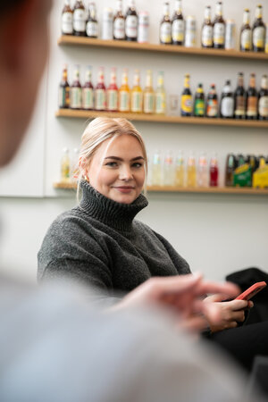 Frau mit hellblonden Haaren, trägt einen Zopf und dunkelgrauen Rollkragenpullover. Sie lächelt in die Kamera.