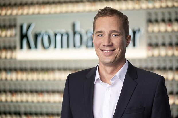 Mann mit kurzen blonden Haaren, trägt einen dunkelblauen Anzug mit weißem Hemd und lächelt in die Kamera.