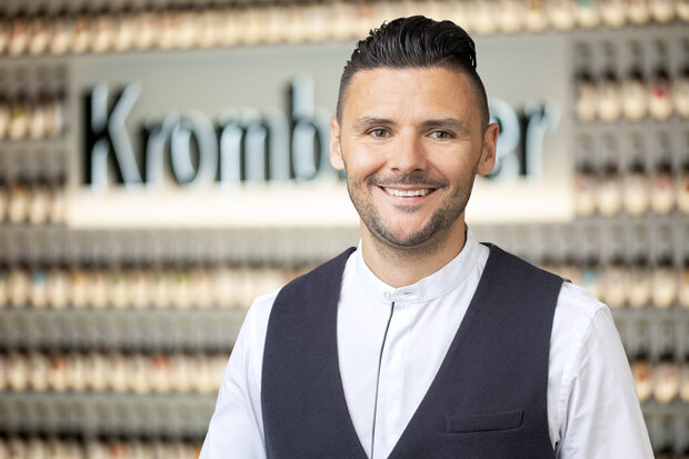 Mann mit schwarzen Haaren trägt eine weiße Bluse und eine schwarze Weste und lächelt in die Kamera.