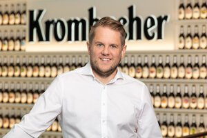Mann mit kurzen blonden Haaren trägt ein weißes Hemd und lächelt.