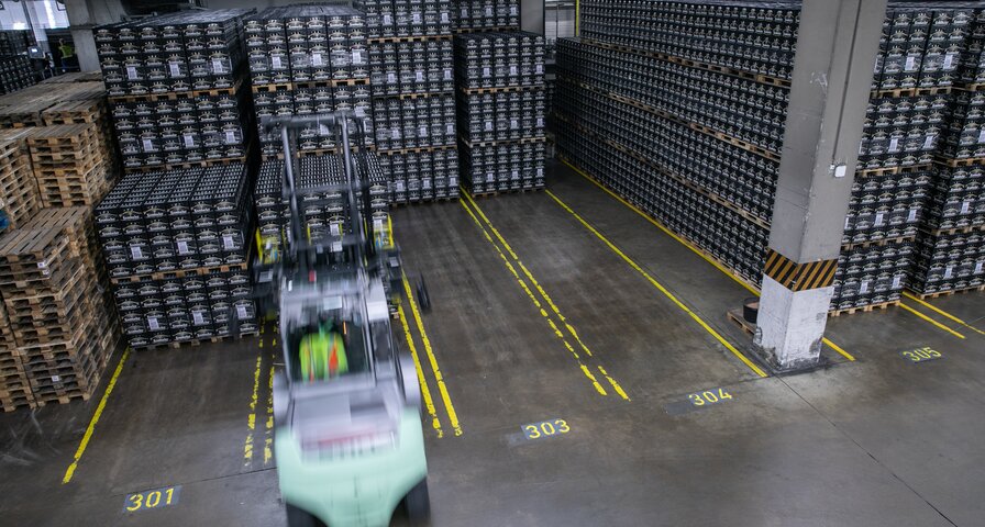 Lagerhalle mit hohen Regalen, ein Gabelstapler stapelt die Kisten.