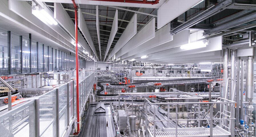 Blick auf eine moderne Produktionshalle mit mehreren Förderbändern, Maschinen und Metallkonstruktionen. 