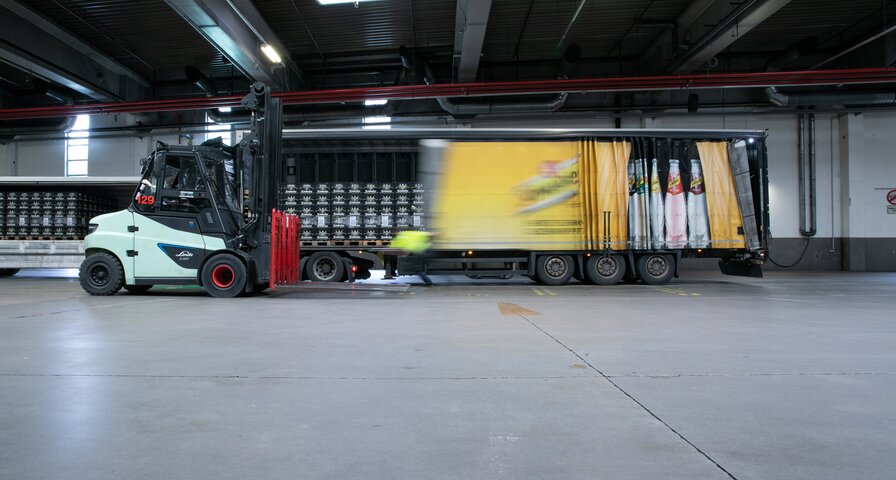 Ein Gabelstapler bewegt sich neben einem gelben Lkw mit Schweppes Werbung. Der Lkw ist teilweise entladen.