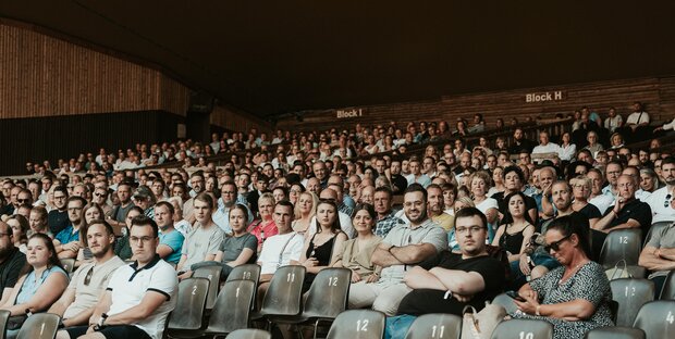 Abbildung von einem großen Saal mit vielen Menschen.