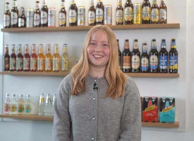 Frau mit langen blonden Haaren, trägt einen hellgrauen Pullover und lächelt in die Kamera.
