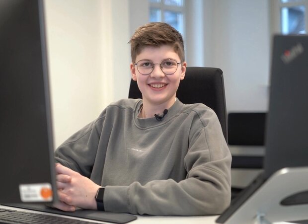 Junger Mann mit hellbraunen Haaren, trägt eine Brille und einen hellgrauen Pullover.
