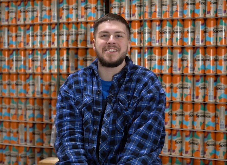 Mann mit kurzen, braunen Haaren trägt ein blau-kariertes Hemd und lächelt in die Kamera.