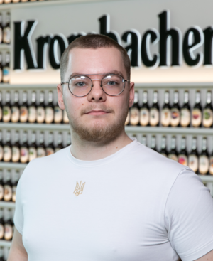 Man mit sehr kurzen Haaren, trägt ein weißes T-Shirt und eine Brille.