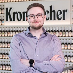 Mann mit kurzen dunkelblonden Haaren, trägt eine Brille und ein blaues Hemd.