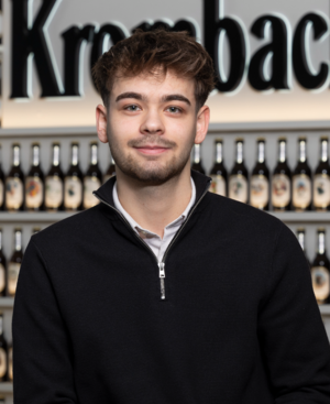 Mann mit kurzen braunen Haaren, trägt einen schwarzen Pullover und lächelt in die Kamera.