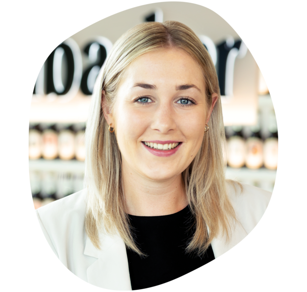 Frau mit schulterlangen, blonden Haaren trägt ein schwarzes Oberteil und einen weißen Blazer. Sie lächelt in die Kamera.