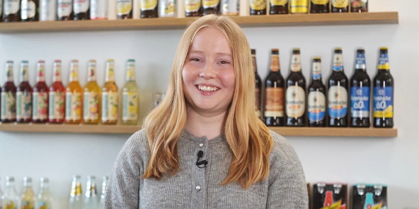 Frau mit langen blonden Haaren, trägt einen hellgrauen Pullover und lächelt in die Kamera.