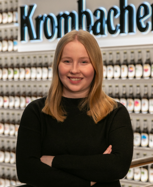 Frau mit schulterlangen, rötlichen Haaren trägt einen schwarzen Pullover und lächelt in die Kamera.