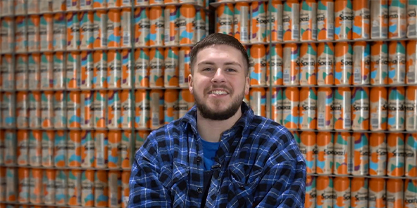 Mann mit kurzen, braunen Haaren trägt ein blau-kariertes Hemd und lächelt in die Kamera.