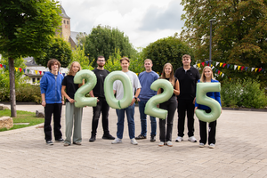 Eine Gruppe von jungen Menschen steht in im freien und halten grüne Luftballon-Zahlen hoch. Die Zahlen zeigen '2025'.