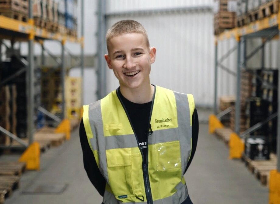 Junger mit hellblonden Haaren, trägt eine Warnweste und lächelt in die Kamera.