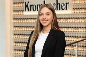 Frau mit langen, blonden Haaren trägt ein schwarzes Blazer und ein weißes T-Shirt. Sie lächelt in die Kamera.