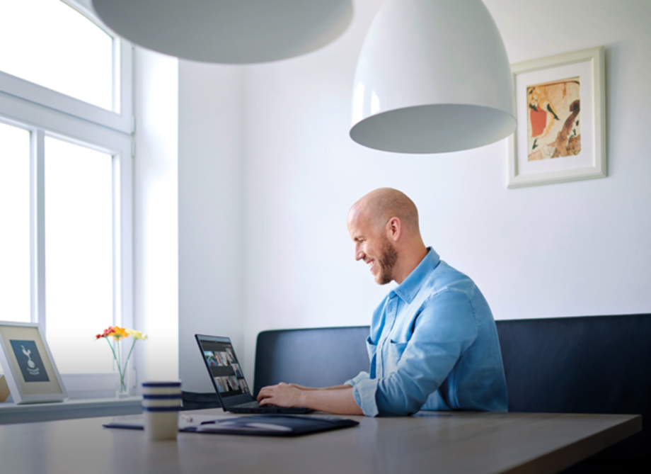 Ein Mann mit Glatze sitzt an einem Tisch und arbeitet an einem Laptop. Er trägt ein hellblaues Hemd. 