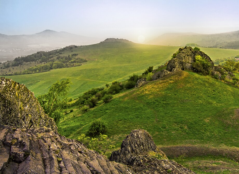 Blick von einem Aussichtspunkt von einem Berg auf Wiesen in der Abendsonne.