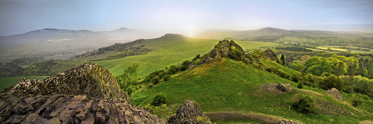 Blick von einem Aussichtspunkt von einem Berg auf Wiesen in der Abendsonne.