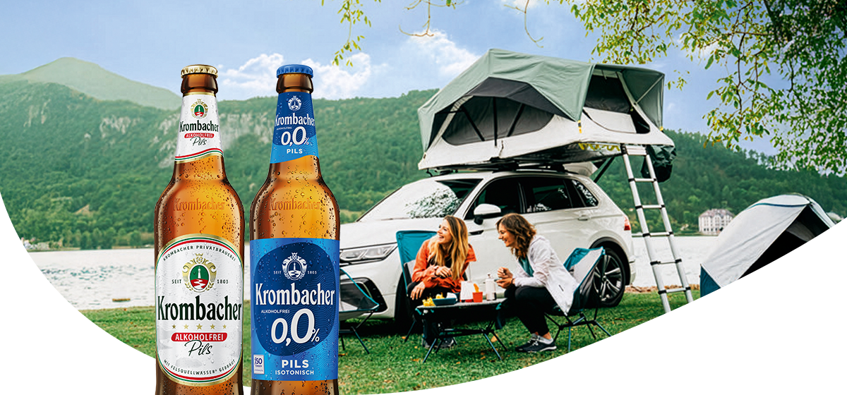 Zwei Krombacher Flaschen und im Hintergrund ein Auto mit Dachzelt und zwei lachenden Frauen.