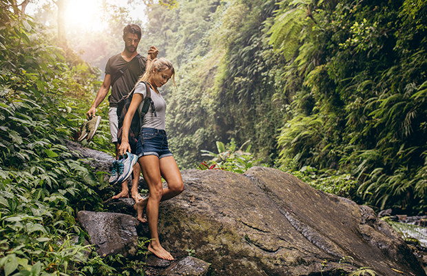 Ein Mann und eine Frau laufen Barfuß in einem Wald über einen Felsen.