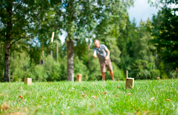 Ein Mann spielt Kubb auf einer grünen Wiese.