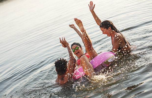 Drei Menschen mit einem Badering sind glücklich in einem See und halten die Hände hoch vor Freude.