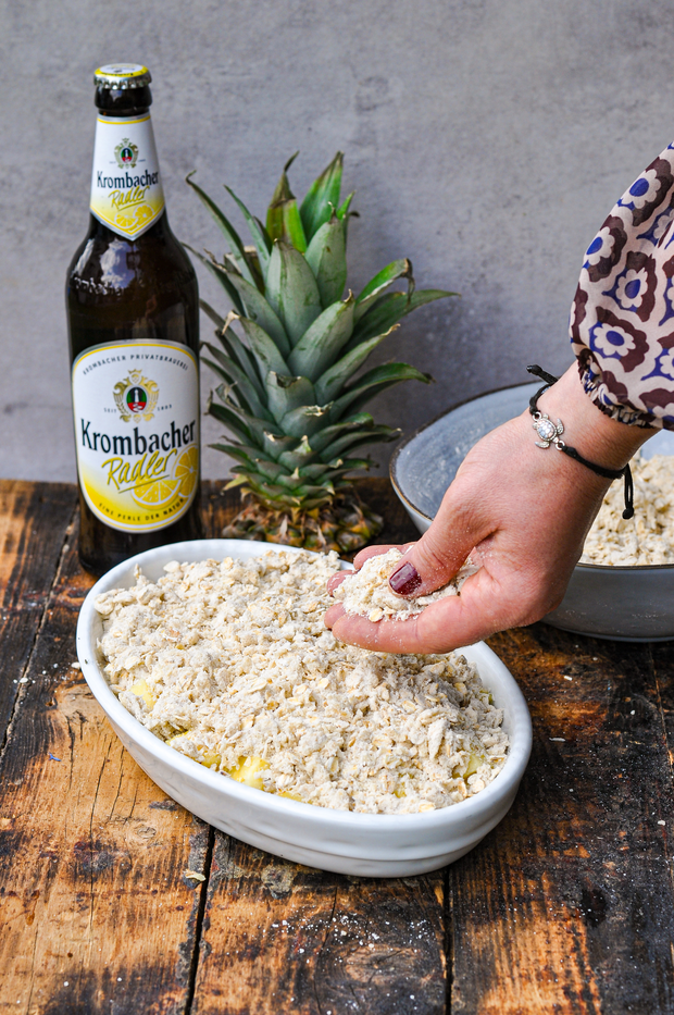 Der Crumble wird gleichmäßig auf die Ananas gestreut.