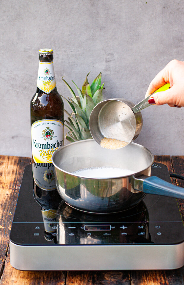In eine Pfanne mit Kokosmilch wird brauner Zucker hinzugegeben.