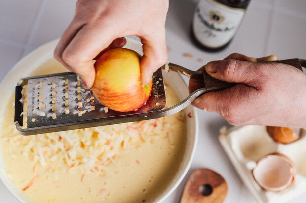 Geriebene Apfelstücke werden zum Kuchen hinzugegeben.